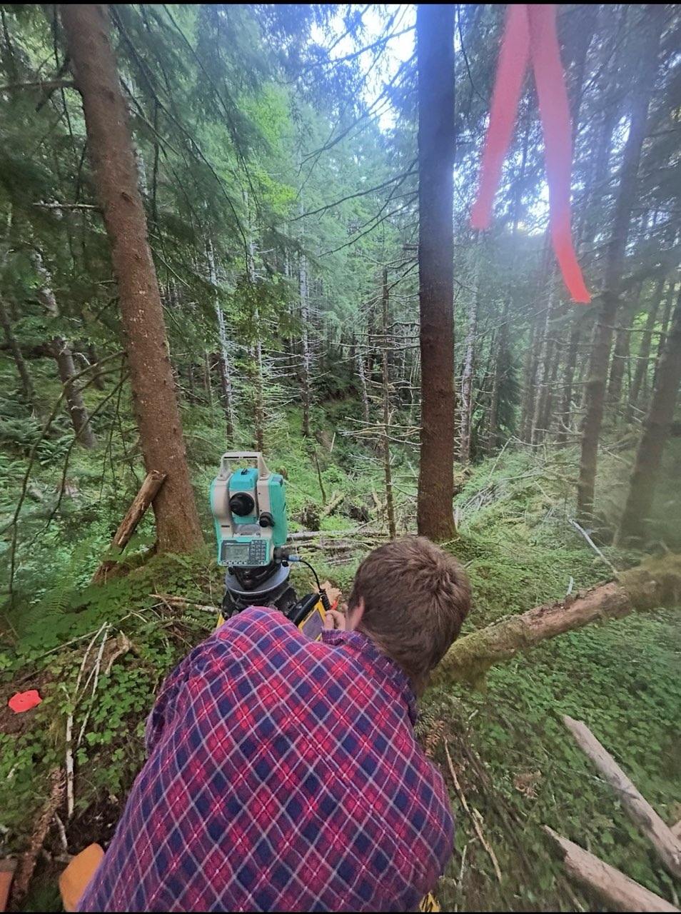 Surveyor operating a total station in dense forest terrain