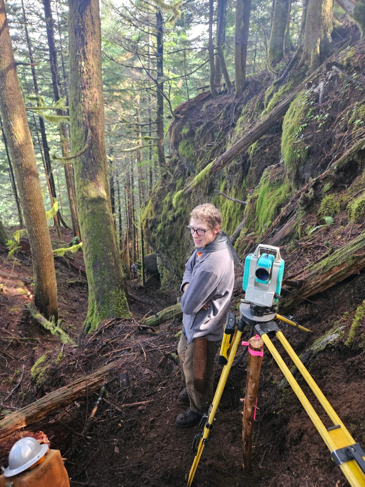 KLS surveyor working with a total station on steep forest terrain