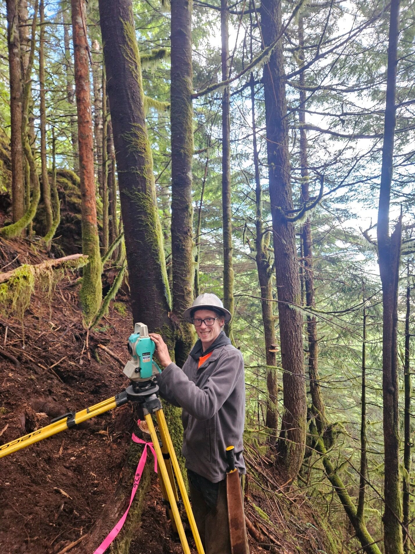 KLS surveyor operating a total station on a wooded hillside