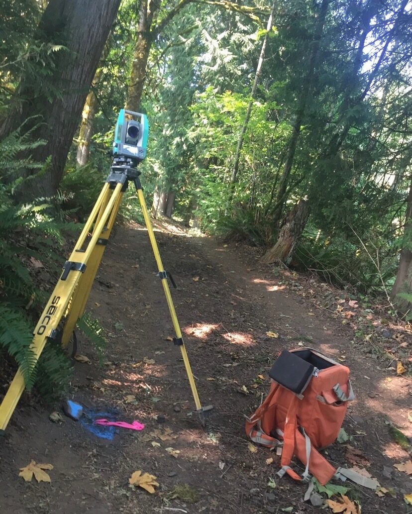 Total station and field pack set up along a wooded trail